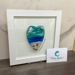A conical shaped sea scene heart in a white frame, with 'Colours of Cornwall' text up the right side of the piece. Left view of the product.