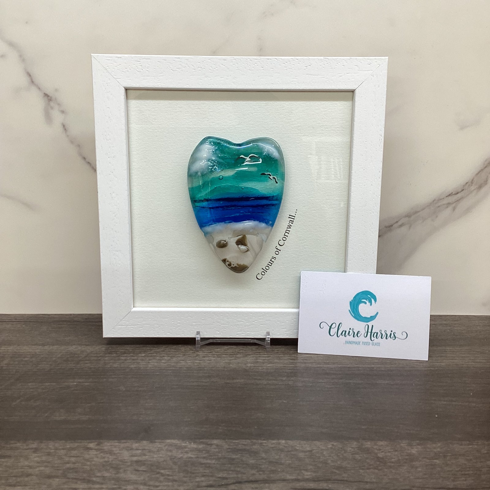 A framed decorative piece featuring a conical shaped sea scene heart with the text 'Colours of Cornwall' up the side. 
