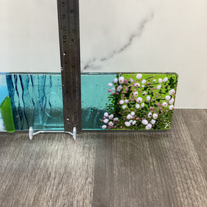 Fused glass large hanger with sea pinks, with a ruler depicting the measurement of the width of the piece. 